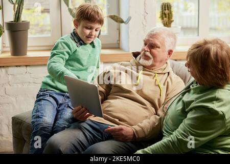 Ritratto di vita di famiglia amichevole, nonno e il loro nipote seduti sul divano e passare del tempo insieme, utilizzando gadget moderni, parlando, studiando Foto Stock