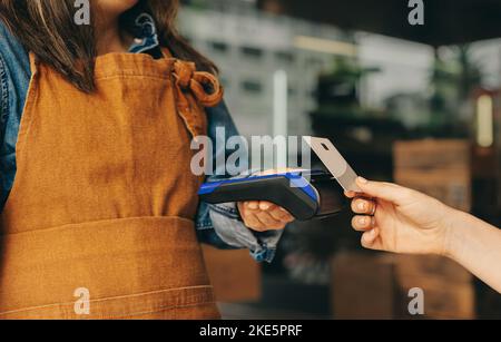 Cliente femmina che scannerizza la sua carta di credito su una macchina di carte per pagare la sua fattura in un caffè. Donna irriconoscibile che fa una transactio senza contanti e contactless Foto Stock