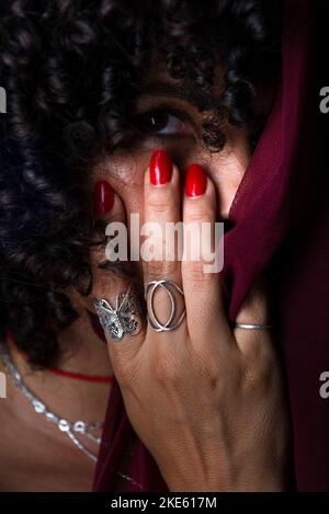 Primo piano ritratto di donna con un panno rosso trasparente sul volto su sfondo nero. Donna matura. Concetto di autostima. Foto Stock