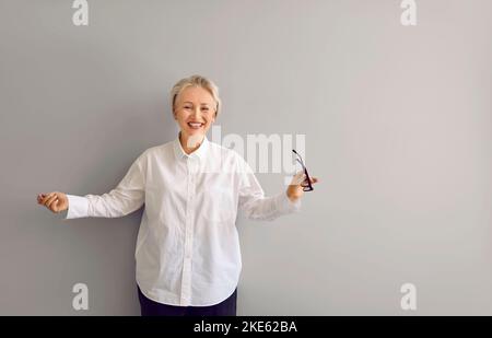 Ritratto di emotivo, felice, gioioso ed elegante donna anziana contro la parete grigia. Foto Stock