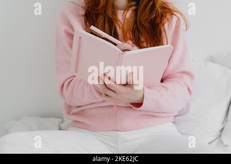 Immagine ritagliata di una donna seduta sul letto e scritta nel notebook. Foto Stock