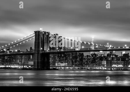 Una vista del Ponte di Brooklyn, sull'East River, in bianco e nero, con uno skyline di Manhattan sullo sfondo Foto Stock