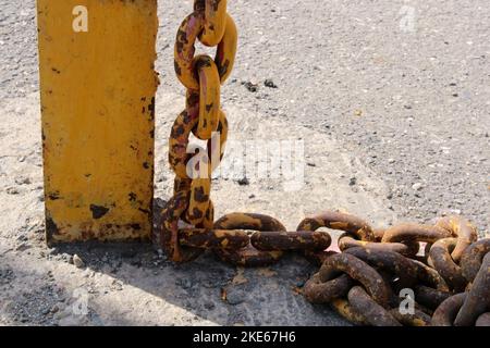 Vecchia catena gialla arrugginita con maglie grandi in primo piano su un rack sul dock. Foto Stock