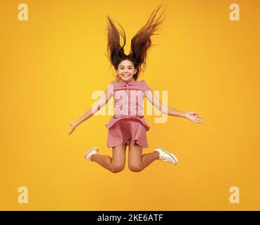 Ragazza teen stupita. Foto full size di salto teen girl positivo con movimento abito estate, moda bambini vestito isolato su sfondo giallo. Adolescente Foto Stock