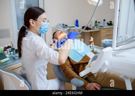 Donna dentista durante il trattamento di un paziente. Il medico effettua il trattamento dentale sui denti di una persona nella sedia del dentista. Messa a fuoco selettiva. Foto Stock