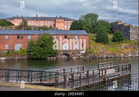 Helsinki, Finlandia - 19 luglio 2022: Fortezza di Suomenlinna. Grandi edifici rossi sulle colline dell'isola orientale sotto il paesaggio blu. Acqua di mare sulla parte anteriore con w Foto Stock