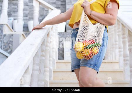 Anonimo donna che tiene il sacchetto della maglia pieno di frutta e di verdure. Foto Stock