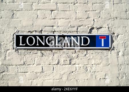 Cartello con il nome della strada di Longland su un muro di mattoni dipinti di bianco Foto Stock