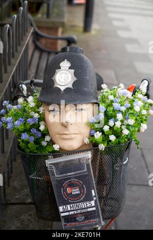 Testa fittizia con casco di un poliziotto in un cesto su una bicicletta con fiori che pubblicizzano un'azienda locale Foto Stock