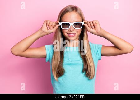 Foto di allegro dolce piccolo bambino indossare t-shirt turchese braccia occhiali scuri sorridendo isolato sfondo di colore rosa Foto Stock