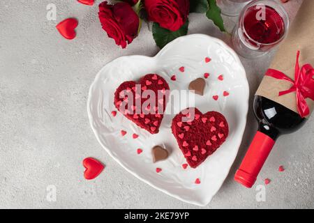 Torte velluto rosso a forma di cuori su un piatto bianco, rose e vino per San Valentino, vista dall'alto Foto Stock