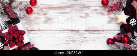 Accogliente Natale o inverno bordo doppio con maglione rosso, nero e beige, scatola regalo, candela, rami di albero gelido e decorazione su sfondo di legno bianco Foto Stock