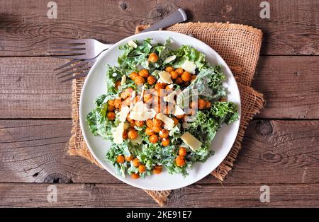 Caesar insalata vegetariana con ceci, kale e un condimento di yogurt. Vista dall'alto tavolo scena su uno sfondo rustico in legno. Concetto alimentare basato su piante. Foto Stock