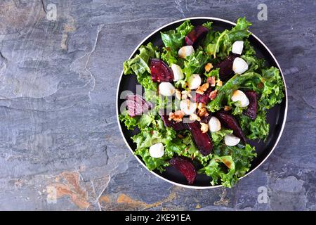 Insalata sana di kale e barbabietole con formaggio e noci. Vista dall'alto su uno sfondo di ardesia scuro. Foto Stock