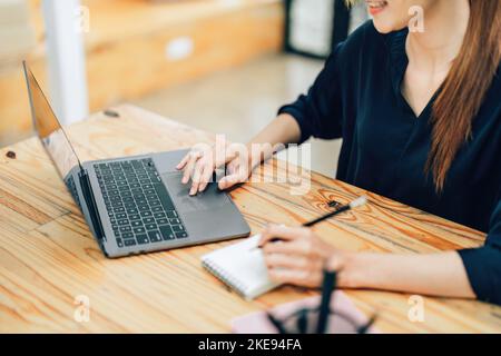 Un ritratto di una ragazza adolescente asiatica che utilizza un computer mentre si siede al lavoro alla ricerca di nuove idee e progetti Foto Stock