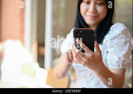 Giovane donna asiatica che usa il suo telefono cellulare, cercando alcune informazioni su internet, messaging suoi amici mentre si agghiacciano al bar. Immagine ritagliata Foto Stock