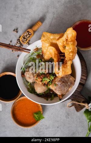 Bakso o polpetta indonesiana servita con zuppa di brodo, tofu, noodle e wonton fritto o gnocchi su un recipiente bianco Foto Stock