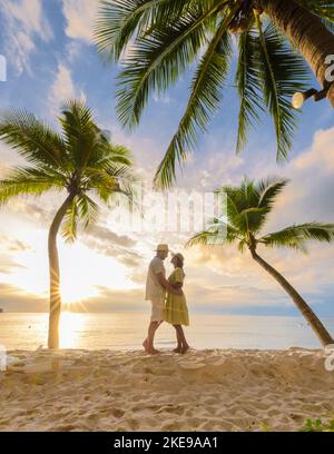 Un paio di uomini e donne che guardano il tramonto sulla spiaggia con sabbia bianca e palme, Bang Tao Beach Phuket Thailandia al sole serale Foto Stock