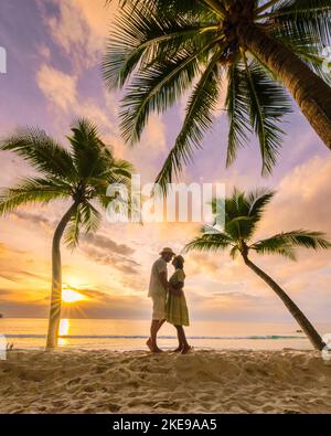 Un paio di uomini e donne che baciano fanno l'amore guardando il tramonto sulla spiaggia con sabbia bianca e palme, Bang Tao Beach Phuket Thailandia. Foto Stock