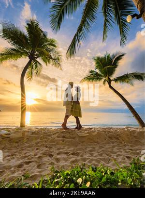 Un paio di uomini e donne che baciano fanno l'amore guardando il tramonto sulla spiaggia con sabbia bianca e palme, Bang Tao Beach Phuket Thailandia. Foto Stock