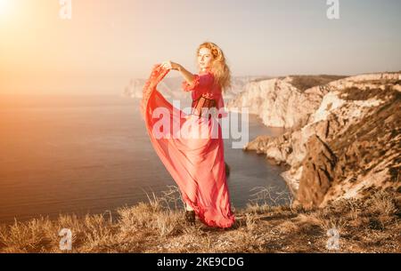 Donna caucasica ricurly rossa con greckles. Bella ragazza bionda giovane carina in un abito rosa lungo posato su una roccia vulcanica alta sopra il mare Foto Stock