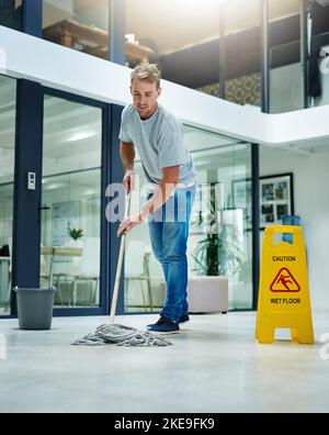 Attenzione scivoloso quando bagnato. Un giovane uomo che pulizia il pavimento dell'ufficio. Foto Stock