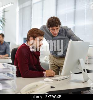 Due menti sono meglio di una: Un uomo d'affari e il suo collega che lavorano insieme su un computer in ufficio. Foto Stock