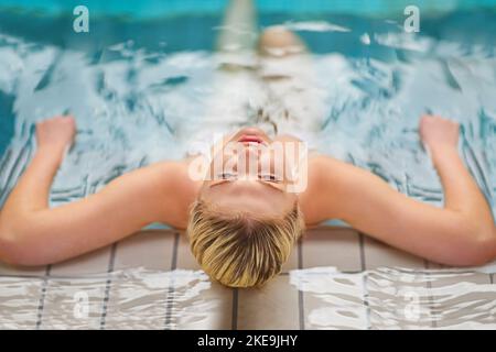 Risparmiate una giornata per rilassarvi. Ripresa di una giovane donna che si rilassa in piscina presso un centro benessere. Foto Stock