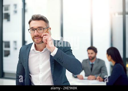 Offrire qualche consiglio professionale. Ritratto di un uomo d'affari che parla su un cellulare durante una riunione del consiglio d'amministrazione con i colleghi sullo sfondo. Foto Stock