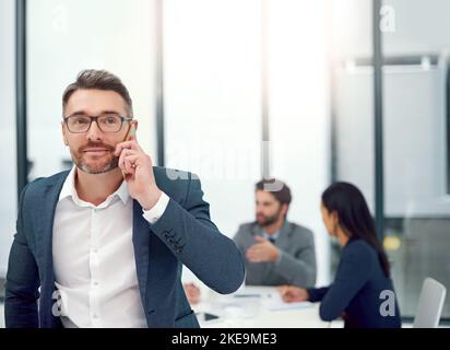 Potrei avere appena la soluzione che avete bisogno... un uomo d'affari che parla su un telefono cellulare durante una riunione del consiglio d'amministrazione con i colleghi nel background. Foto Stock