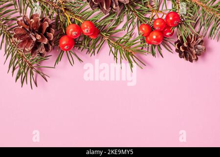 Composizione natalizia di rami di abete, coni e bacche di rowan su sfondo rosa con spazio copia Foto Stock