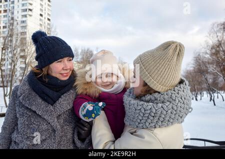 Nonna, madre e figlia camminano nel parco invernale della città durante le vacanze di Natale e Capodanno. Genitori e bambini piccoli che si divertono all'aperto Foto Stock