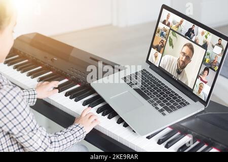 Musicista giovane e grazioso che suona il pianoforte digitale classico a casa durante la lezione online a casa, distanza sociale durante la quarantena, autoisolamento, online Foto Stock