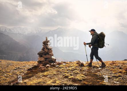 Uomo turista Hiker con grande zaino in silhouette sulla collina contro cielo nuvoloso nella valle di montagna. Esterno e trekking concetto. Foto Stock