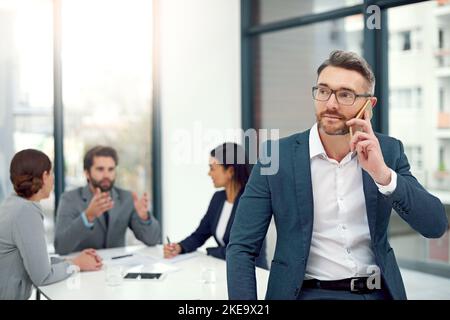 Appreaciate la vostra chiamata. Un uomo d'affari che parla su un telefono cellulare durante una riunione del consiglio d'amministrazione con i colleghi in background. Foto Stock