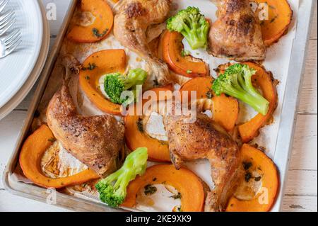 Arrostire il pollo con zucca kuri rossa e broccoli su una teglia da forno Foto Stock