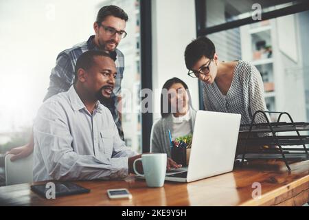 Theres nessun bisogno di farlo da solo quando avete una squadra. Inquadratura ad angolo basso di un gruppo di uomini d'affari riuniti intorno a un notebook in ufficio. Foto Stock