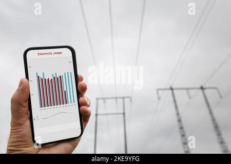 Mano con smartphone e linea di alimentazione in background Foto Stock