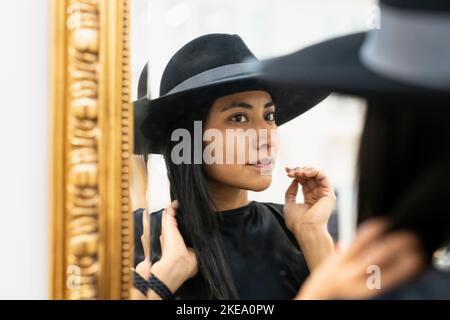 Giovane donna in cappello nero che guarda in specchio Foto Stock