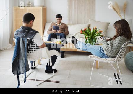 Adolescenti seduti nel soggiorno e che utilizzano telefoni e tablet Foto Stock