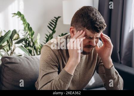 Primo piano di stress triste giovane uomo sentire dolore avendo terribile forte mal di testa concetto, stanco sconvolto ragazzo caucasico massaggiare templi che soffrono di migra Foto Stock