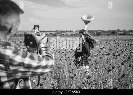 coppia in amore fare foto. uomo con macchina fotografica e donna in campo papavero. estate fiore prato Foto Stock