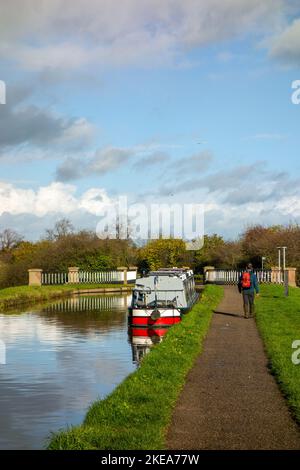 Uomo che cammina lungo l'alzaia del canale sul canale di Unione Shropshire a Nantwich Cheshire verso l'acquedotto progettato da Thomas Telford passando accanto alle barche a remi Foto Stock