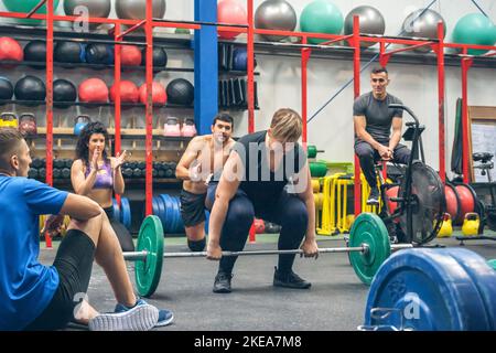 Donna pronta a fare pesi di sollevamento mentre i suoi compagni di palestra che la allietano Foto Stock
