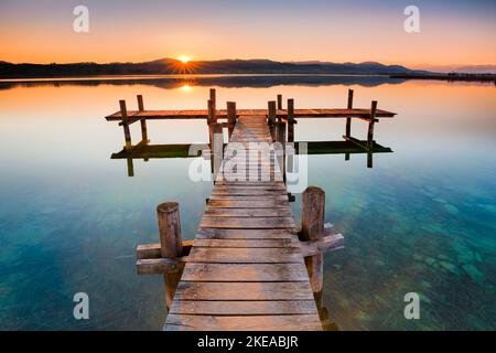 Holzsteg am Pfäffikersee im Gegenlicht bei Sonnenaufgang mit Blick zum Bachtel und Glärnisch im Hintergrund, Pfäffikon, Kanton Zürich, Schweiz Foto Stock