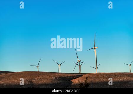 Turbine eoliche multiple in piedi su una collina all'alba e che generano elettricità Foto Stock