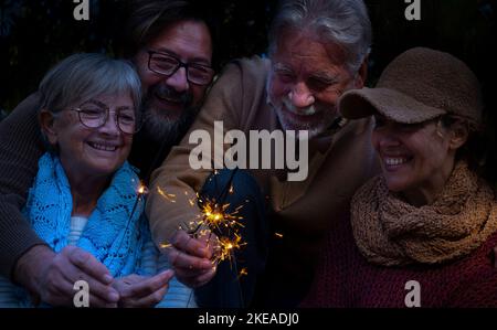 Gruppi di persone in famiglia si godono e festeggiano insieme con una luce scintillante all'aperto. Festa alternativa di nuovo anno per gli uomini e le donne che si divertono. Concetto o Foto Stock