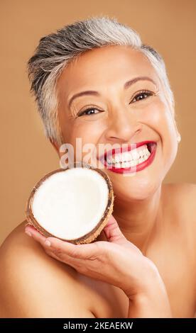 Donna anziana, cura della pelle e cocco in studio per la bellezza, la salute e il benessere in felice ritratto cosmetico. Donna nera sana, anziana e frutta vicino Foto Stock