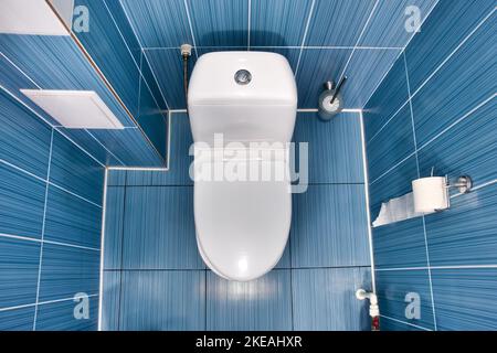bagno bianco con coperchio chiuso in bagno con parete piastrellata blu. Vista della tazza igienica pulita sulla parte superiore con carta igienica. La camera era piccola. Foto Stock