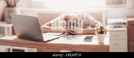 Donna stanca che le mette la testa sulle mani sulla scrivania in ufficio Foto Stock